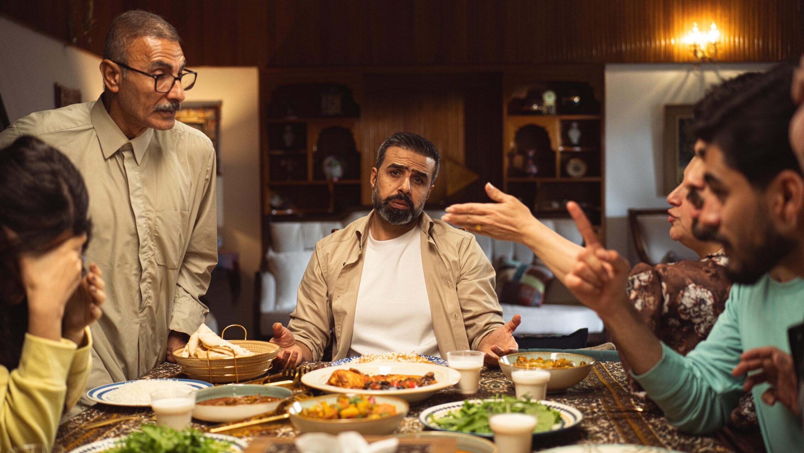 Family Drama: A family engages in a lively discussion around a dinner table filled with dishes.
