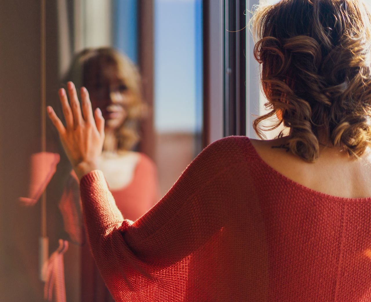 Rear view of a woman in red clothing, looking at her reflection in Madrid and thinking about self-acceptance