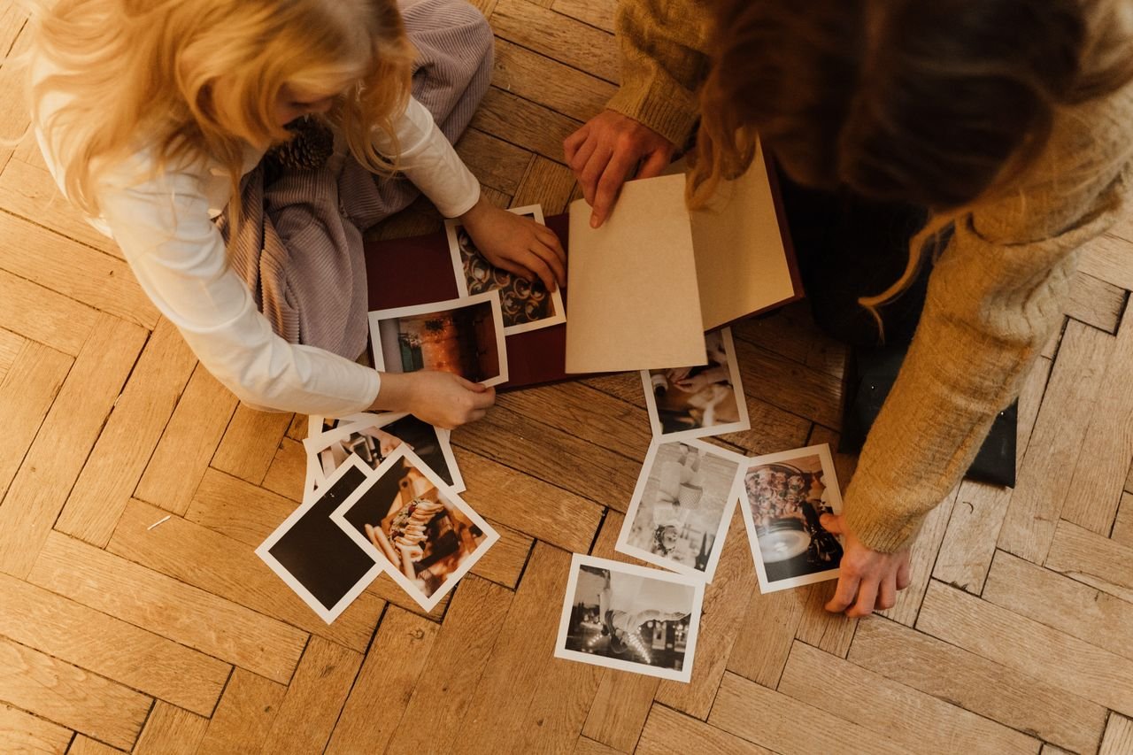 An overhead view of two people sharing and organizing photographs on the wooden floor. Enjoying my own company doesn't mean that I don.t want to be surrounded by loved ones.