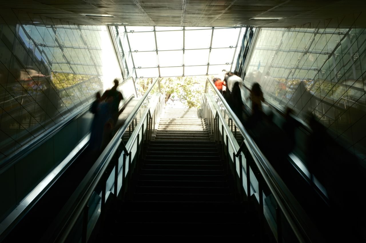 Urban scene of a bustling escalator in İstanbul, Türkiye with dynamic sunlight and modern architecture. Someone looking at the fast pace of life and feeling behind.