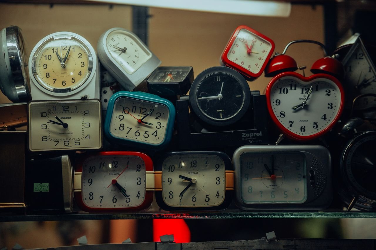 A collection of vintage alarm clocks stacked together, showcasing diverse designs and styles. This indicating the we don't have to be the same version of ourselves with everyone.