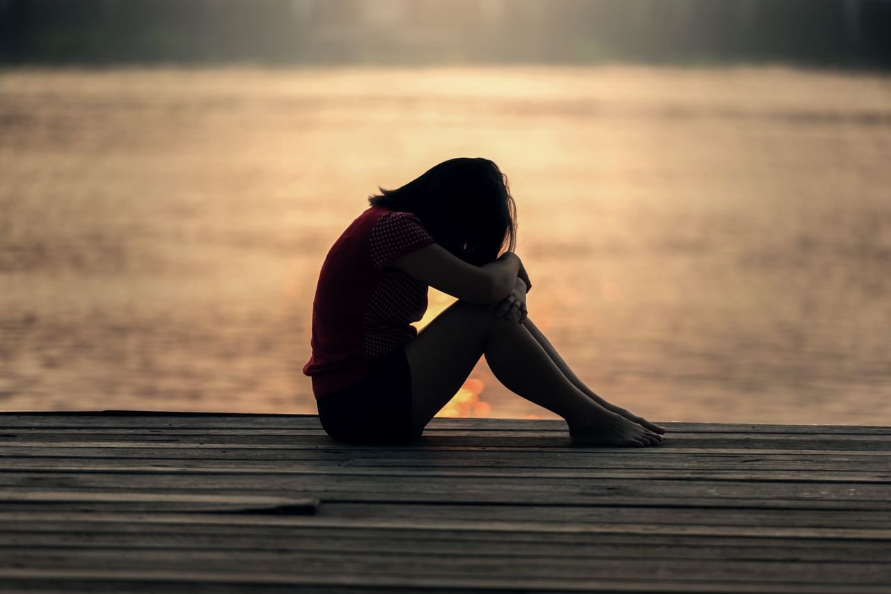 A woman sitting alone on a wooden dock by the lake, showing solitude, reflecting on the fear of regret and wondering if she should have tried.