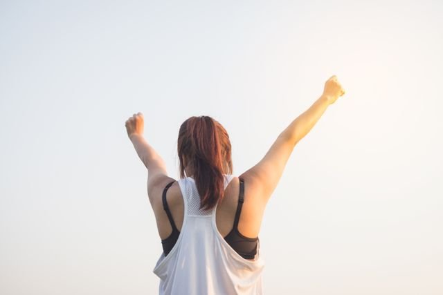 A woman stands outdoors with her arms raised in celebration. Success can come from continuing to move forward even when we don’t feel like it.
